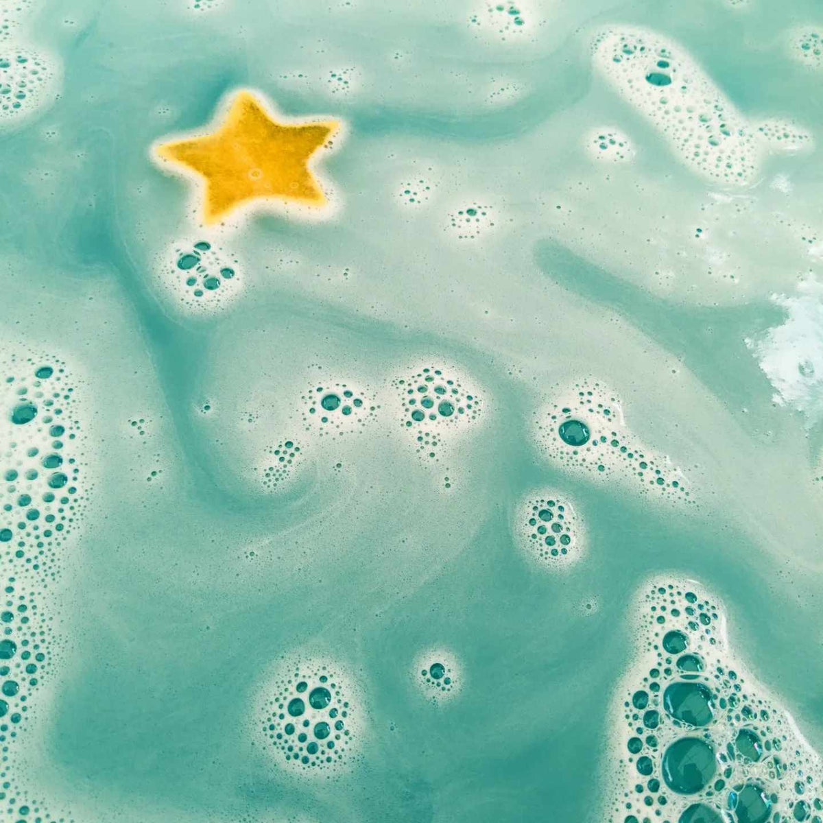 Yellow star sponge toy floating in teal bath water with rainbow swirls
