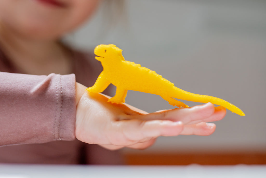 Child's hand holding a yellow lizard sponge toy from an Egg Bath Bomb Sprudel