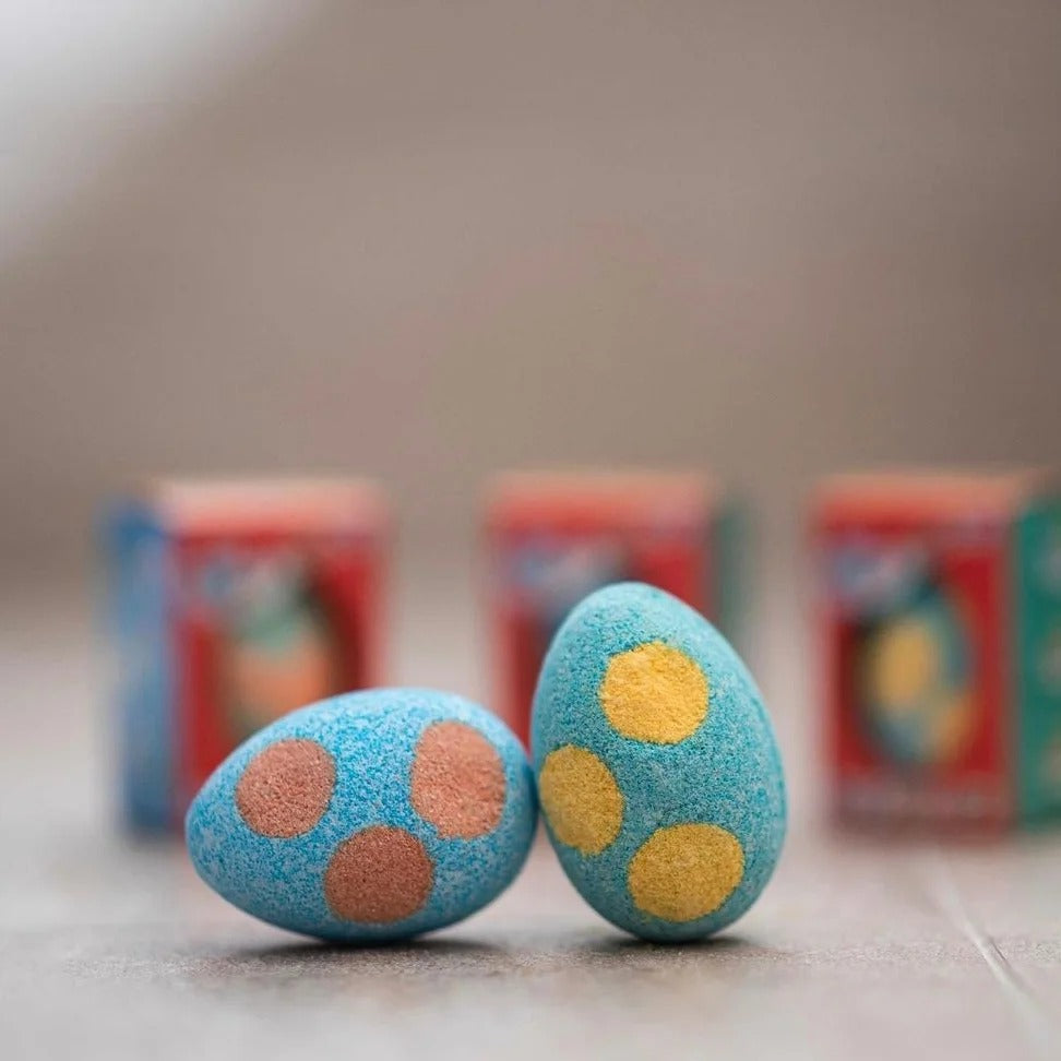 Blue and orange spotted Egg Bath Bomb Sprudels in front of their red packaging