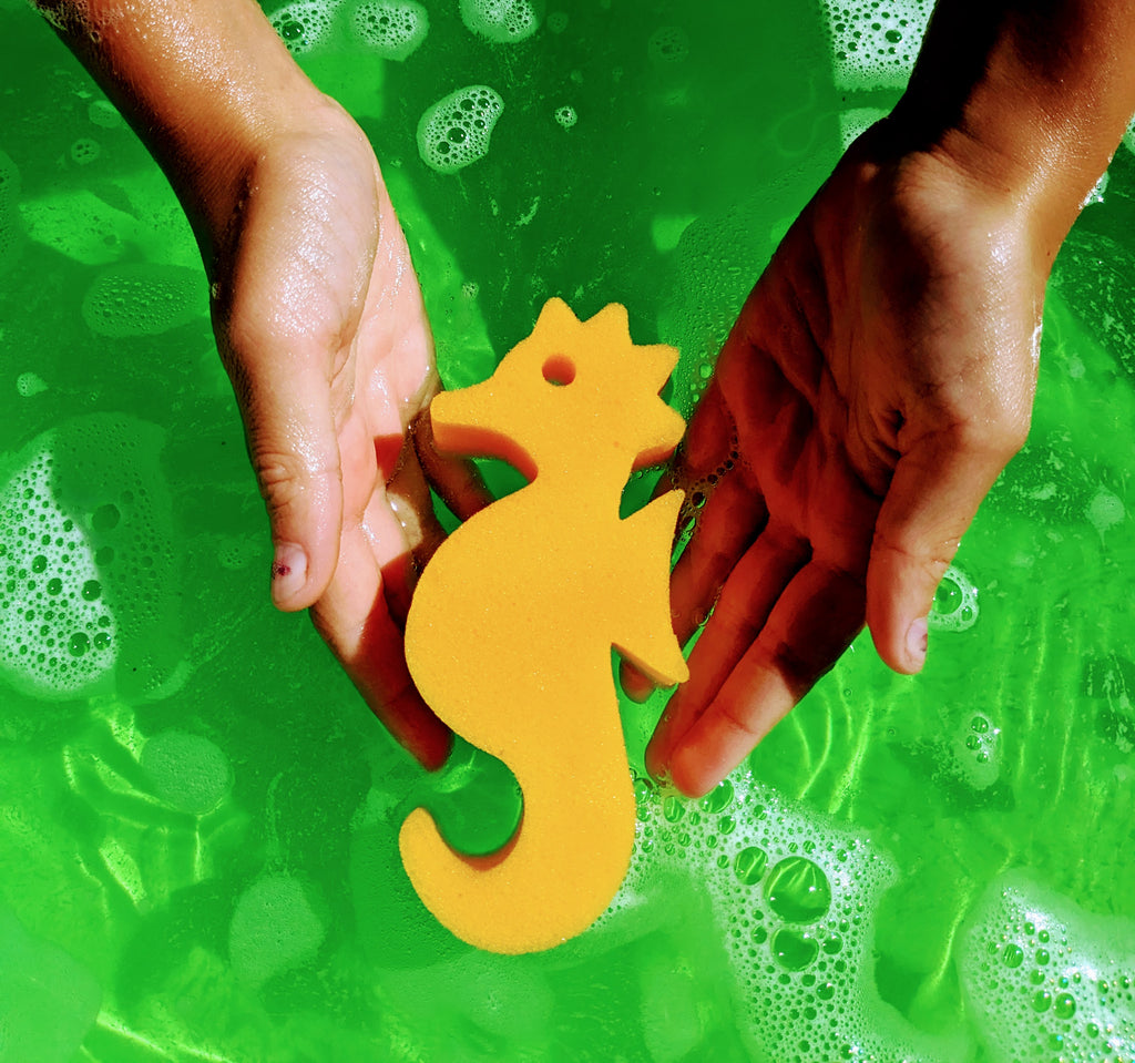 Child's hands holding a yellow seahorse sponge toy in green bath water