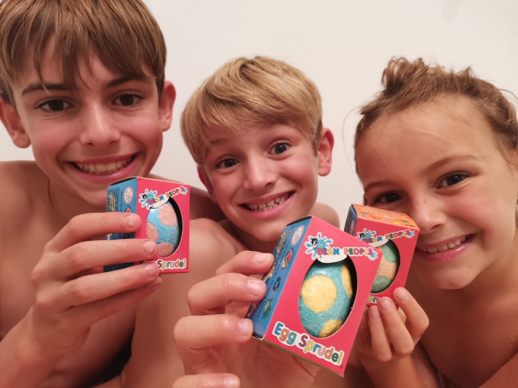 Three smiling kids holding boxed Egg Bath Bomb Sprudels in the bath