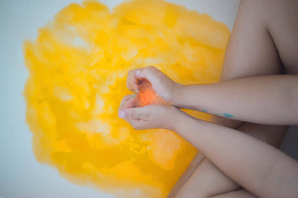 Child's hands in yellow-orange bath water from a fizzing bath bomb