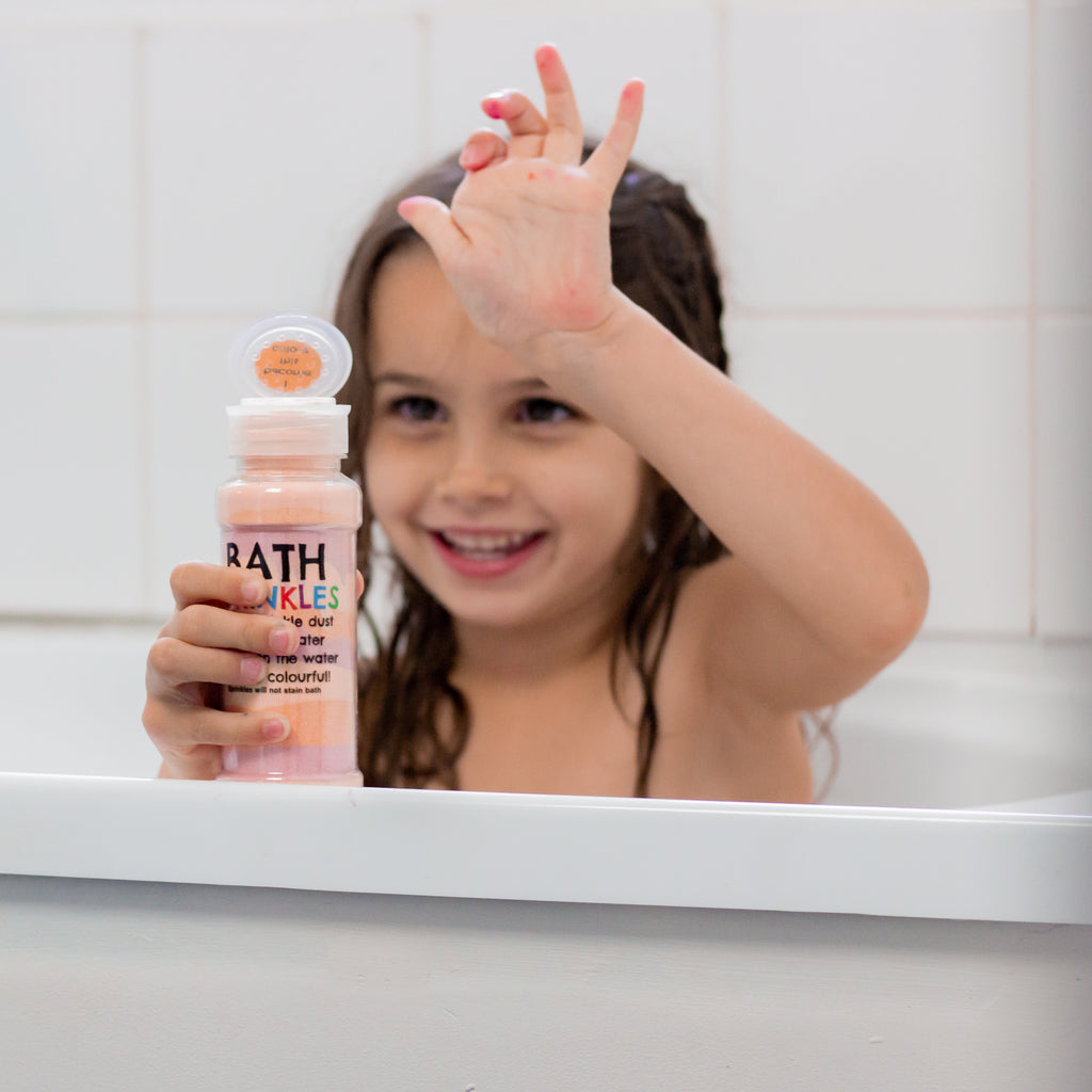 Smiling girl in the bath holding an orange Bath Sprinkles shaker