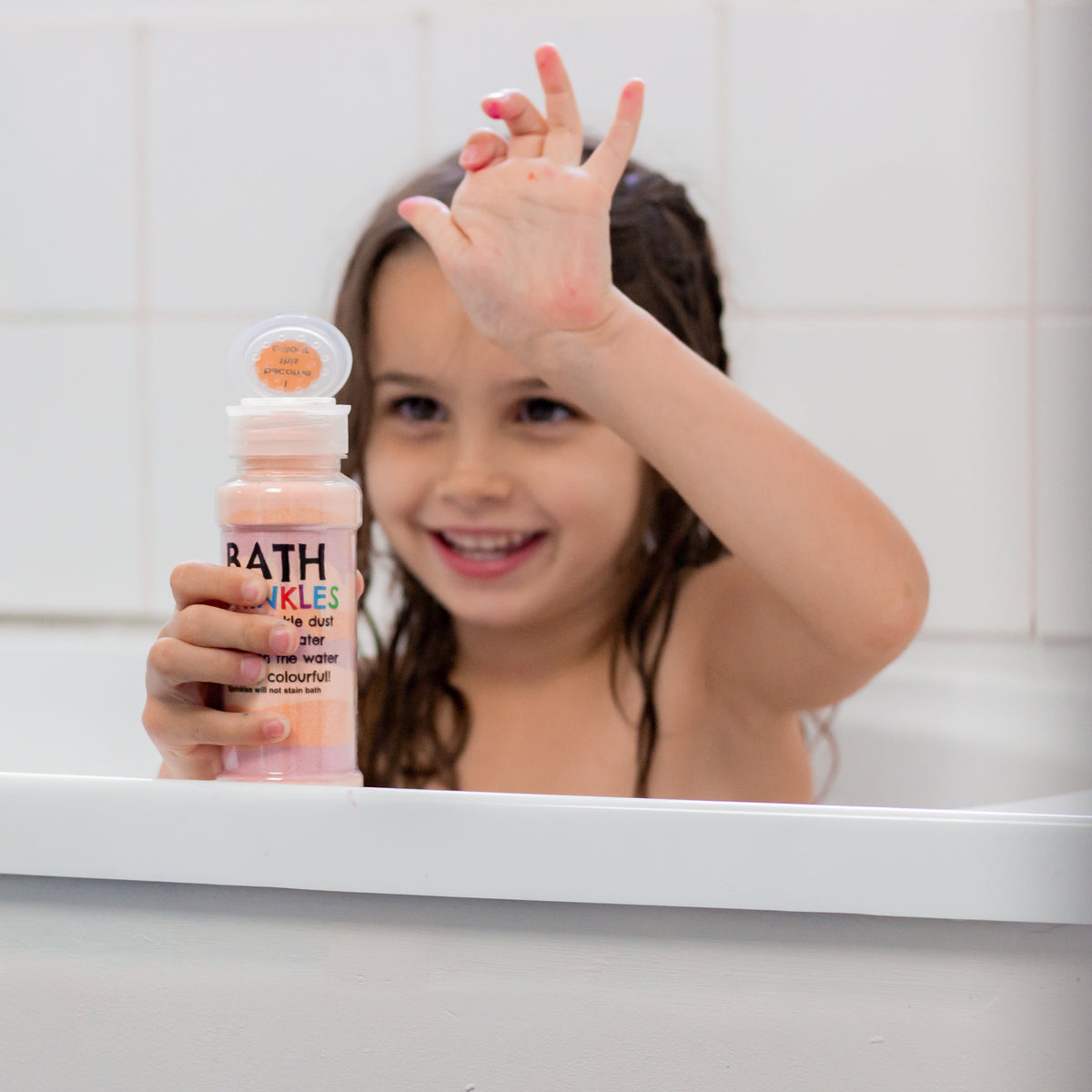Smiling girl in the bath holding an orange Bath Sprinkles shaker