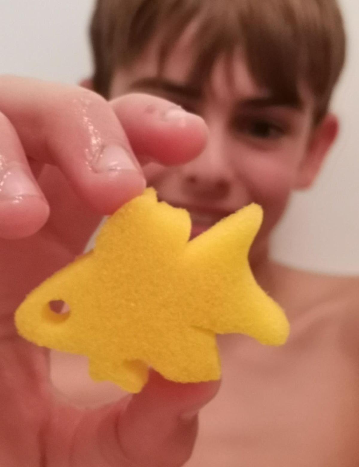 Boy holding up a yellow fish sponge toy from an Egg Bath Bomb Sprudel