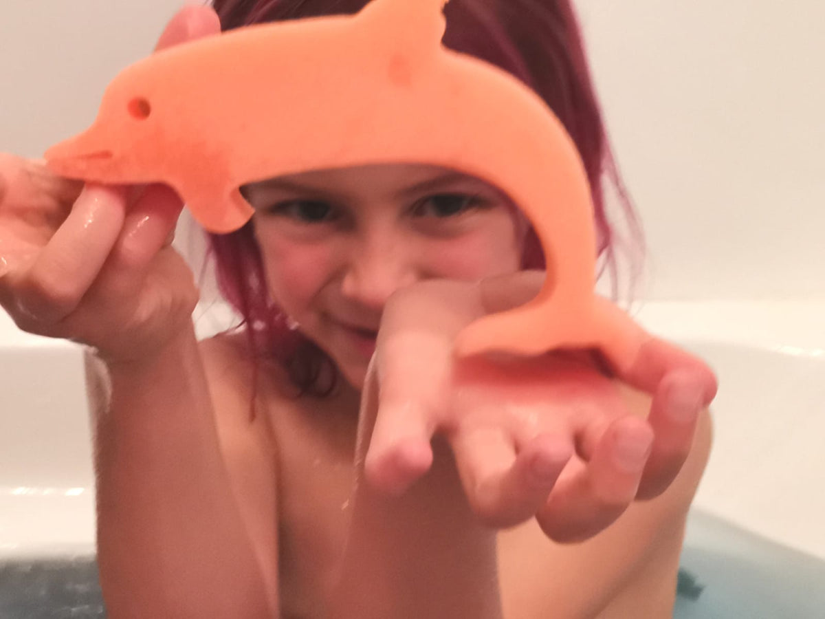 Girl in the bath holding an orange dolphin sponge toy from a Jumbo Bath Bomb Sprudel