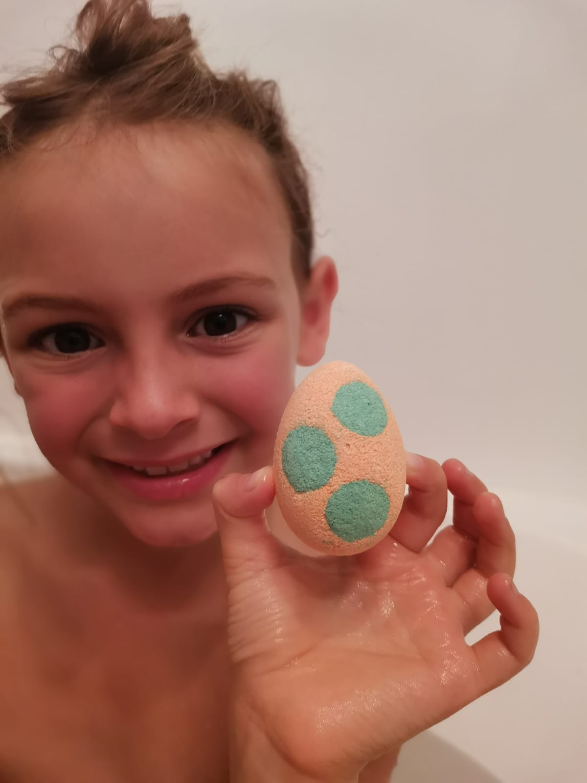 Smiling girl in the bath holding a spotted Egg Bath Bomb Sprudel