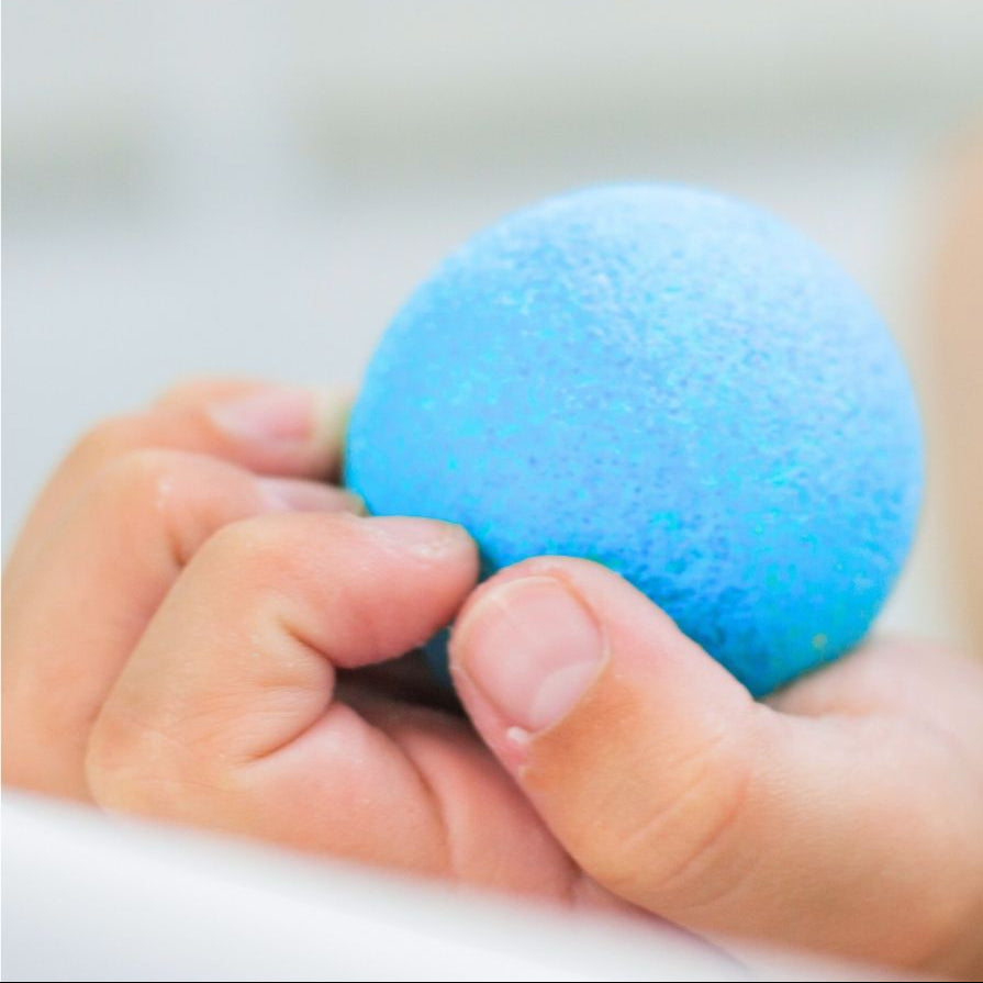 Child’s hand holding a blue kids bath bomb