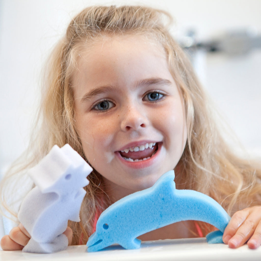 Smiling girl holding a blue dolphin sponge toy and a white sponge toy