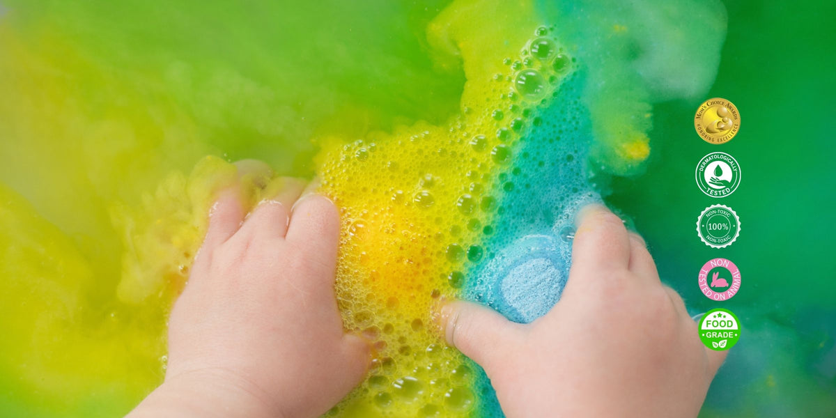 Child’s hands playing in rainbow-coloured fizzing kids bath bomb water